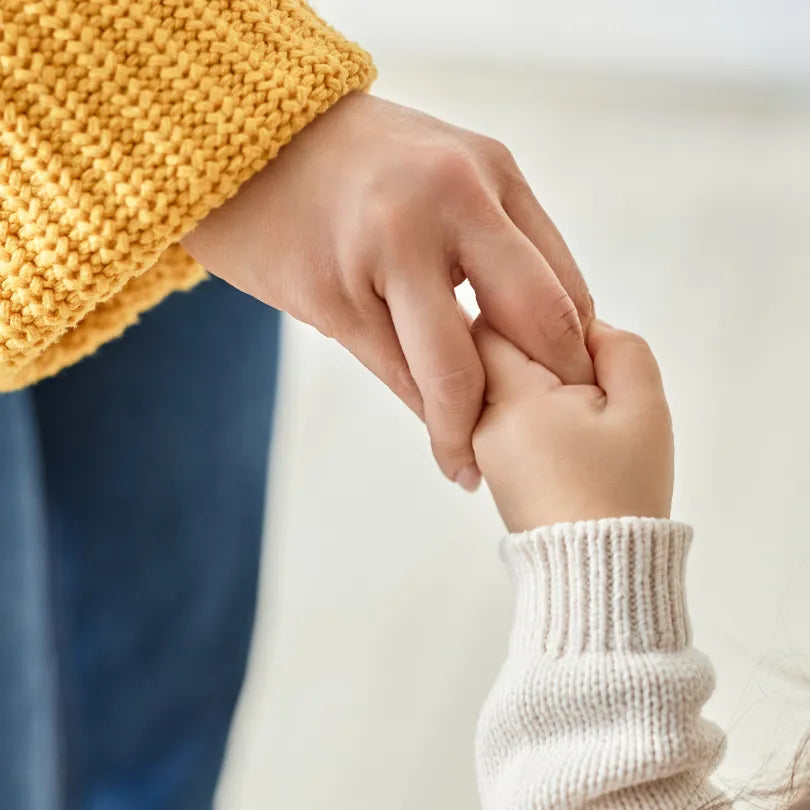  Baby holding a mother's finger against a light gray background.