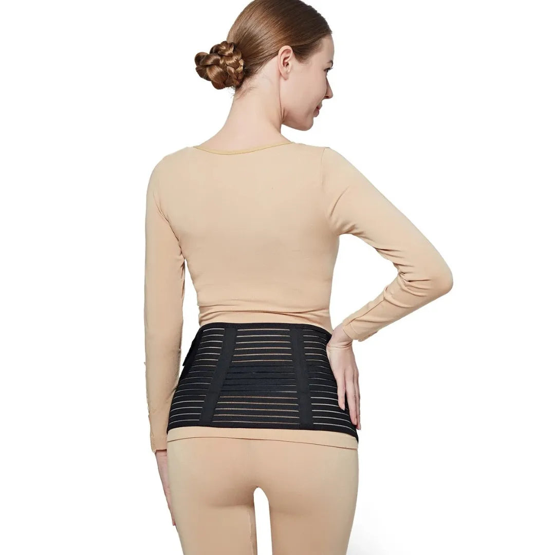 Back view of a pregnant woman wearing a black belly support band for lumbar and lower back support against a white background.