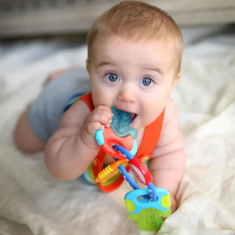 A white 6-month-old baby chewing the teether key with a blurred colored background.